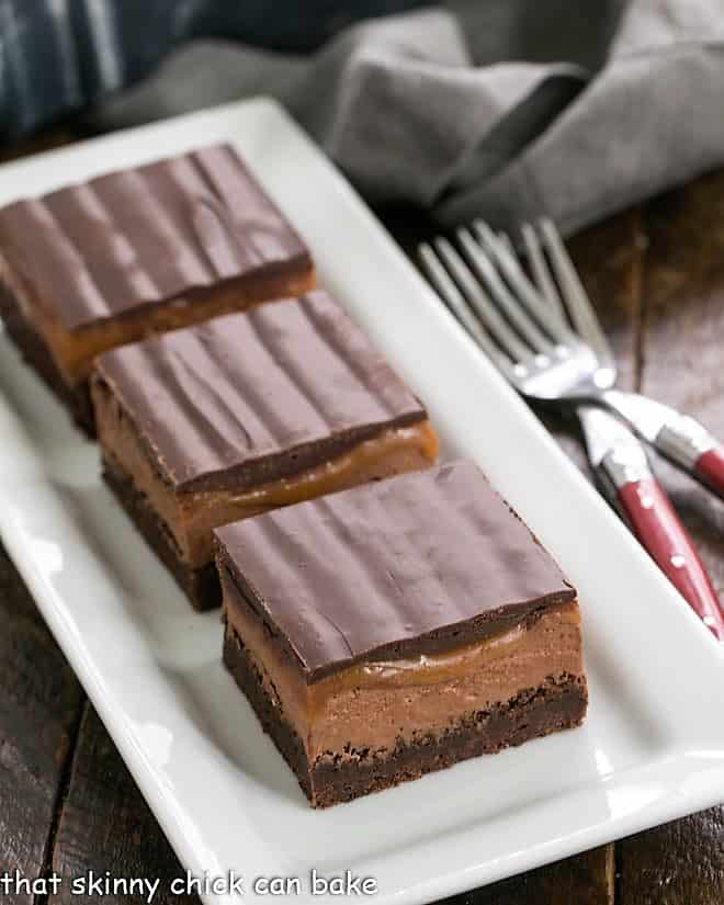 Milky Way Brownies - inspired by the classic chocolate and caramel candy bar! 3 milky way brownies on a white ceramic tray.