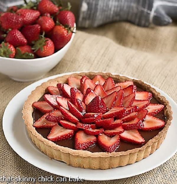 Strawberry Topped Chocolate Tart on a white plate with a bowl of strawberries