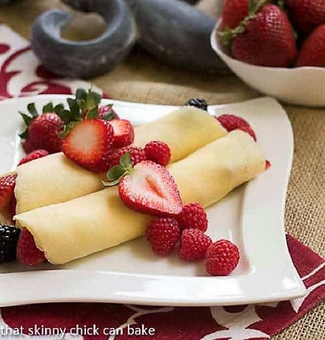 Brown Butter Crêpes with Berry and Cheesecake Filling on a square, wavy white plate.