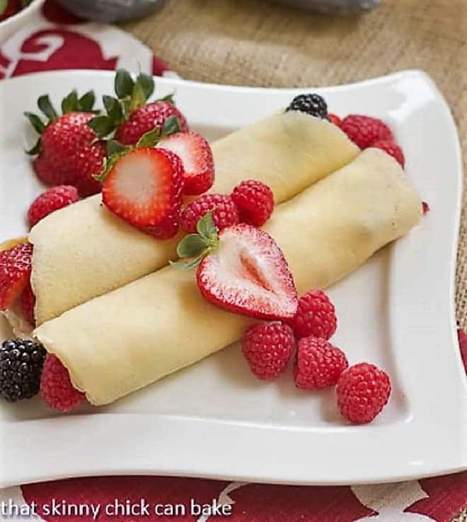 Two Brown Butter Crêpes with Berry and Cheesecake Filling topped with strawberry slices and fresh raspberries.