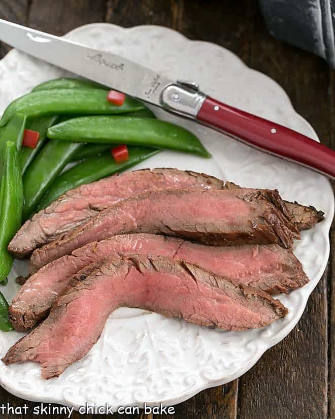 Overhead view of slices of flank steak, sugar snapped peas and a red handle knife.