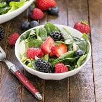 Spinach berry salad in a small white bowl with a red handled fork