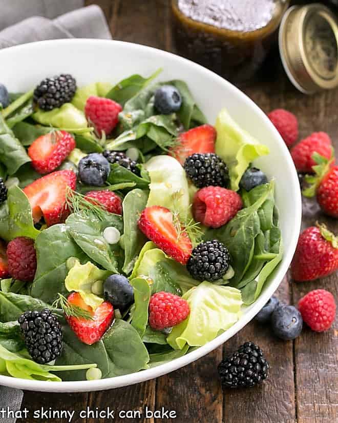 Spinach berry salad in a white ceramic bowl surrounded by fresh berries