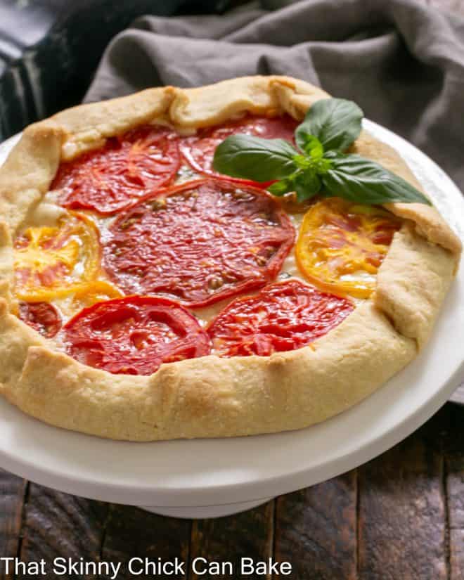 Tomato Galette on a white cake stand with a fresh basil garnish
