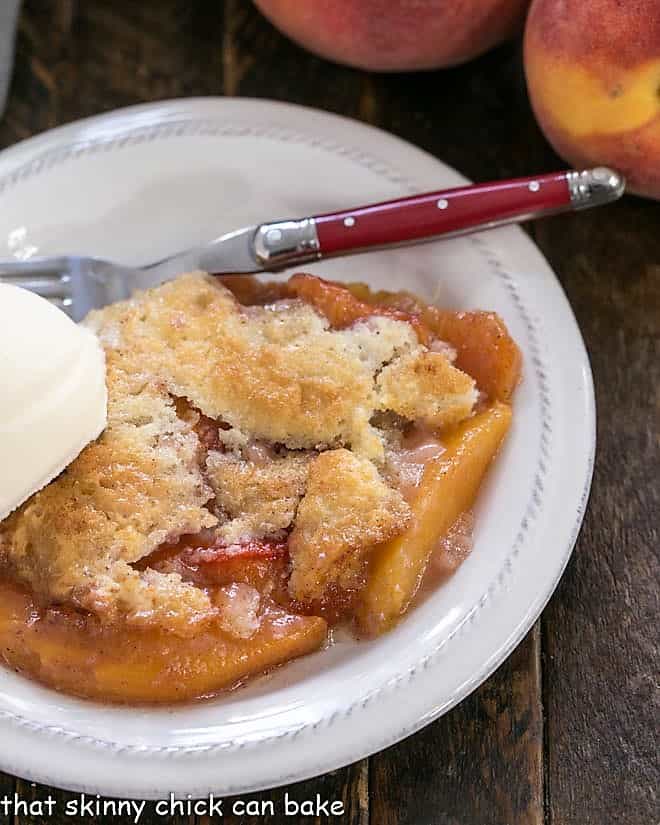 Peach Cobbler on a white dessert plate topped with a scoop of vanilla ice cream