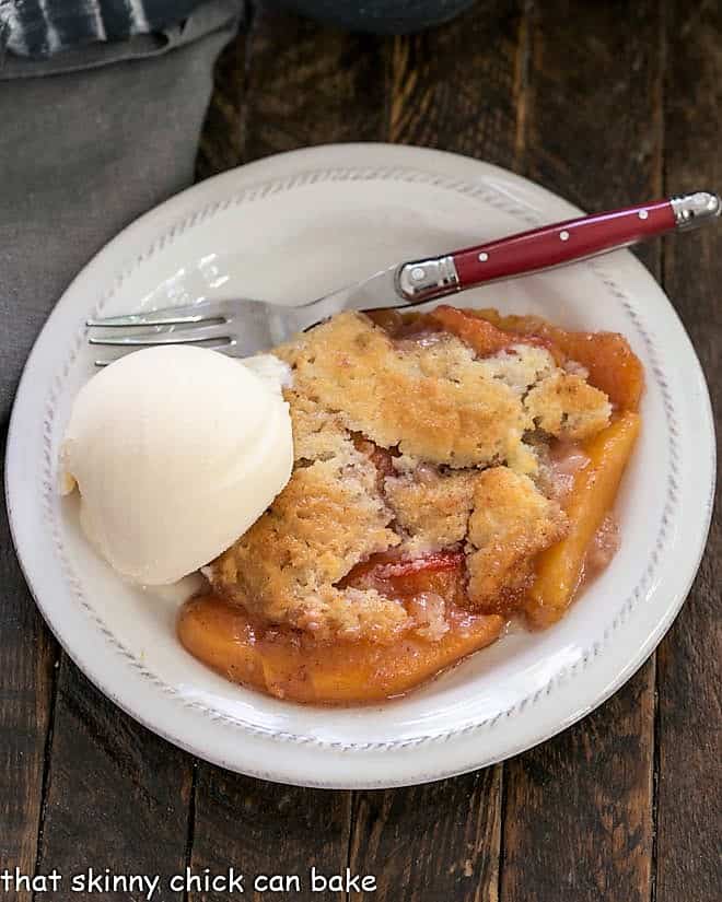 Overhead view of an easy peach cobbler topped with a scoop of vanilla ice cream with a red handled fork.