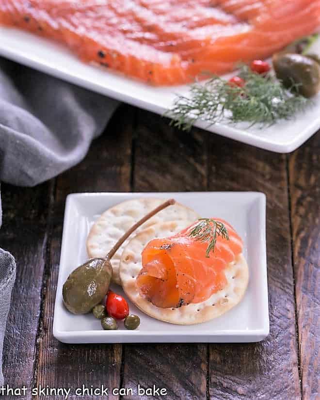 A slice of gravlax on a cracker on a square white plate.