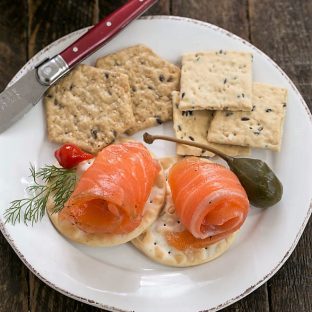 Gravlax on crackers on a small white plate with a red handle knife