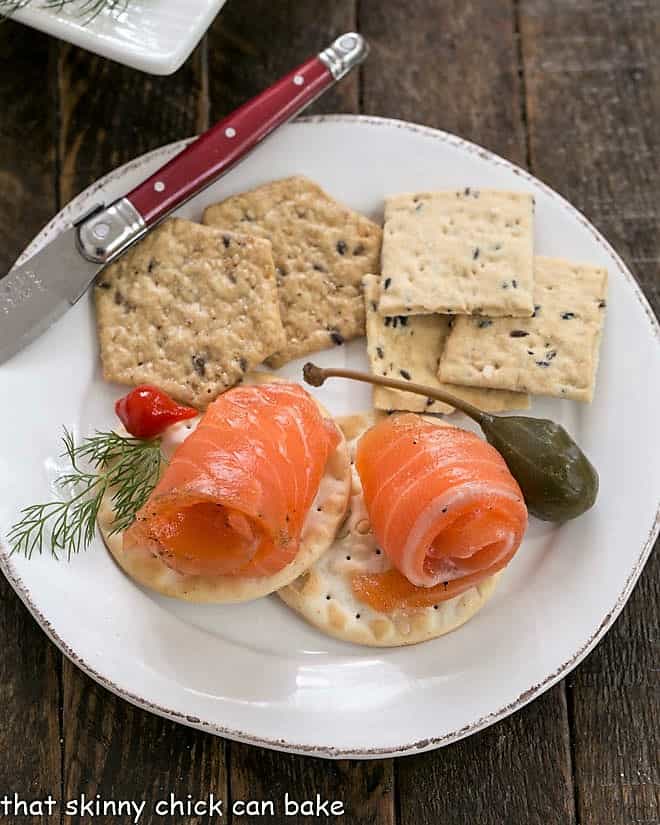 Gravlax on crackers on a small white plate with a red handle knife