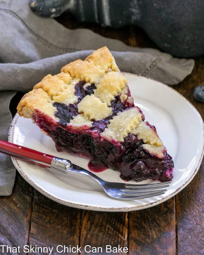 Slice of Lattice Topped Blueberry Pie on a white dessert plate with a red handle fork.