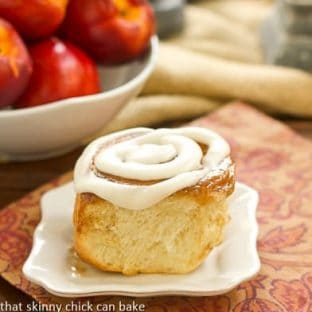 A nectarine cinnamon roll on a white plate over an orange pattern napkin