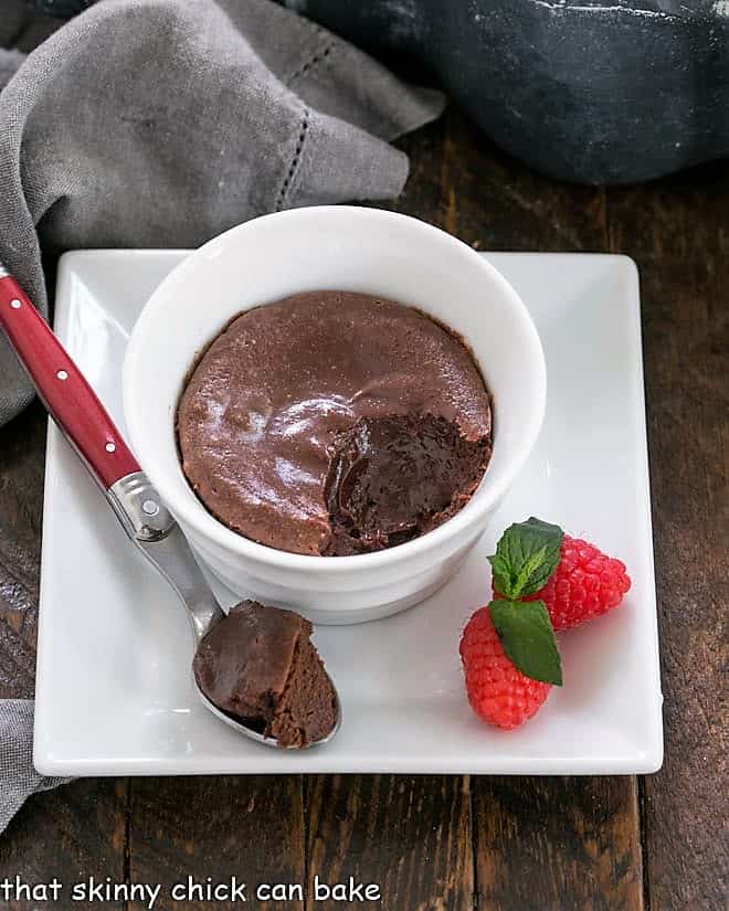 Individual chocolate cheesecake in a white ramekin on a square white plate with a spoonful removed