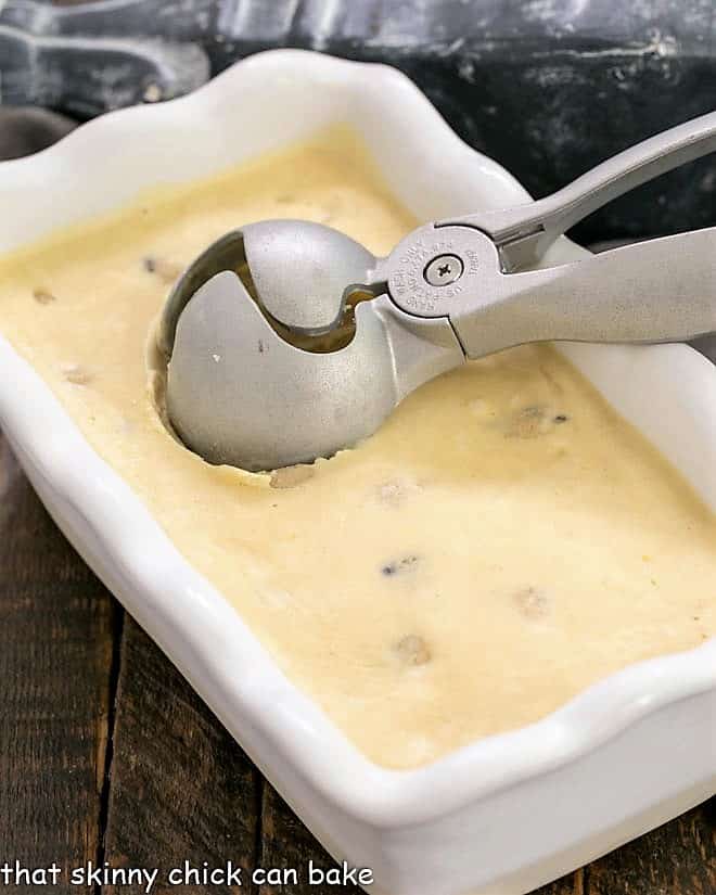 Cookie dough ice cream frozen in a white loaf pan with an ice cream scoop