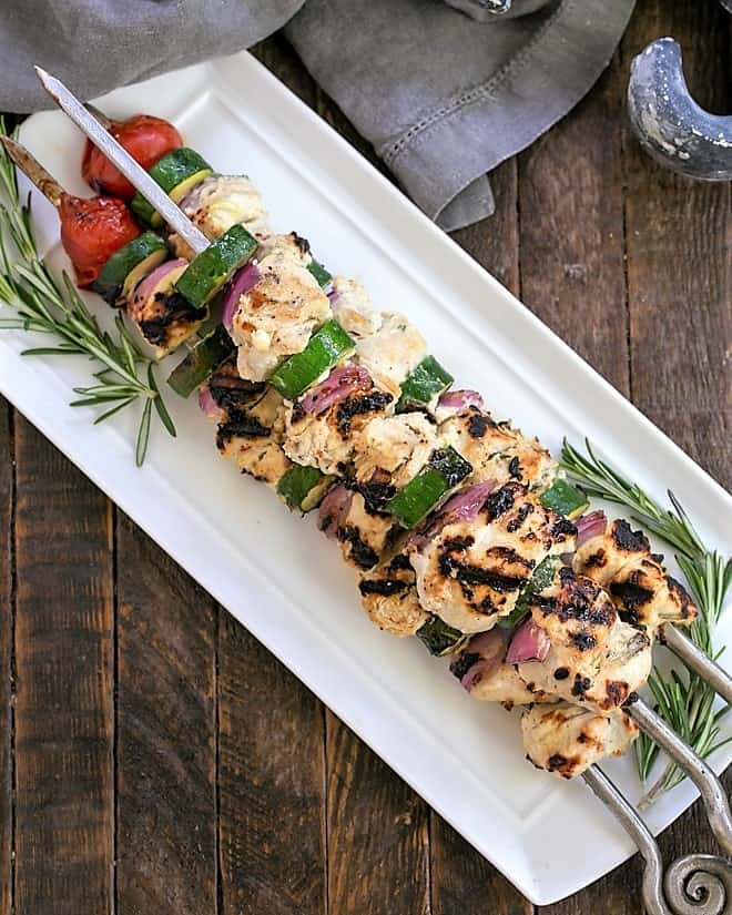 Overhead view of a white platter with grilled chicken kabobs.