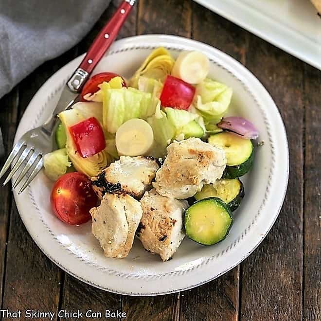 Overhead view of a white plate of grilled chicken kabobs and a green salad.