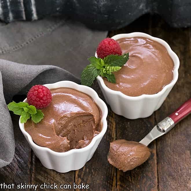 2 white ramekins of chocolate mousse with one spoonful removed