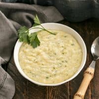 Cheesy polenta in a small white bowl garnished with a sprig of parsley