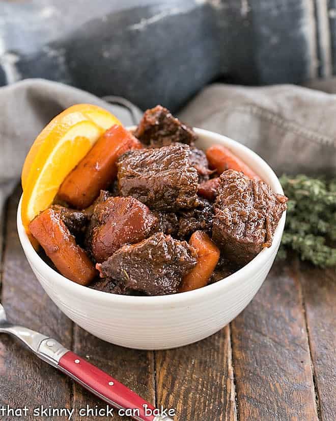 Beef Stew with carrots and orange slices in a white bowl with a red handled fork