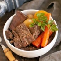 Pot roast garnished with parsley in a white bowl.