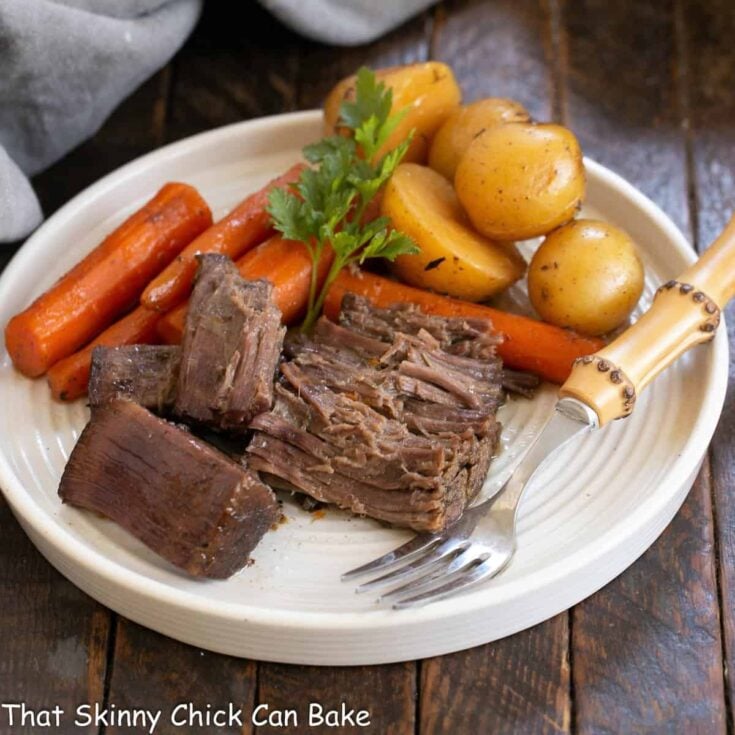 Beef chuck roast and vegetables on a white plate with a fork.