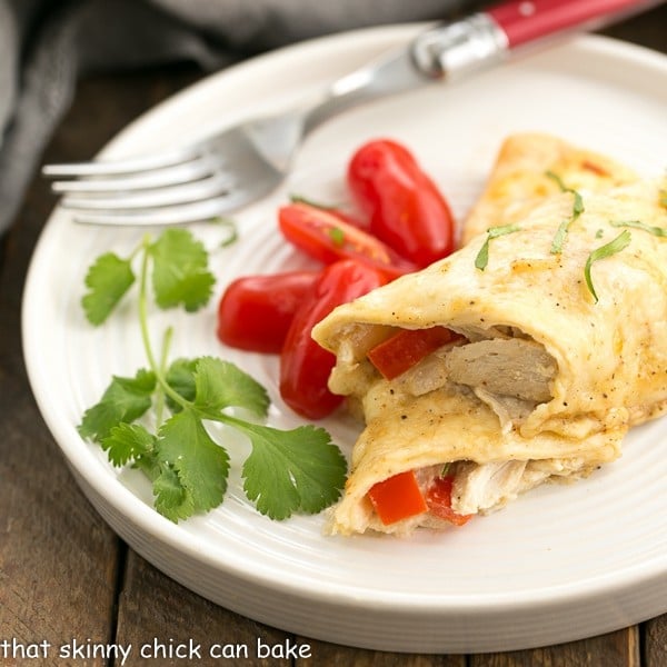 Cheesy Chicken Enchiladas on a white dinner plate with cilantro and grape tomatoes