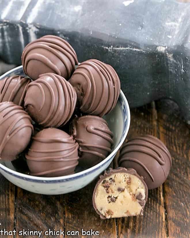 A bowl of cookie dough bites with one whole and one cut open truffle on the side