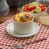 A muenster souffle in a ramekin with a bowl of salad over a red and white napkin