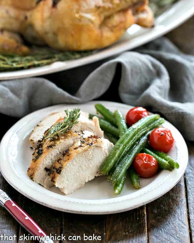 Whole roasted chicken sliced on a white plate with green beans.