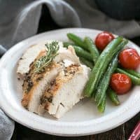 Whole roasted chicken on a white plate with green beans and tomatoes