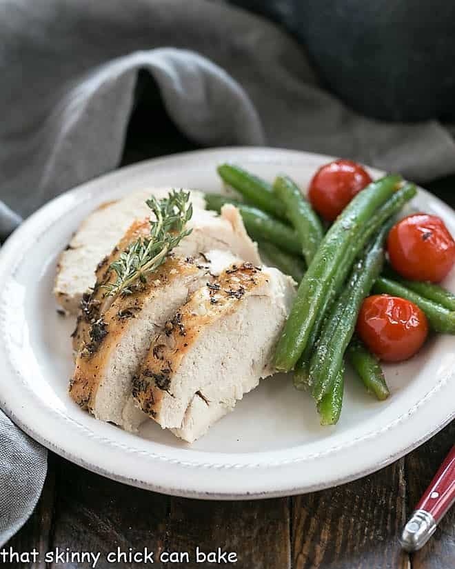 Whole roasted chicken on a white plate with green beans and tomatoes