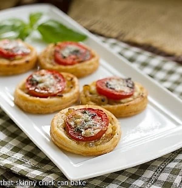 Tomato and Boursin Tartlets lined up on a white ceramic tray with a sprig of basil.