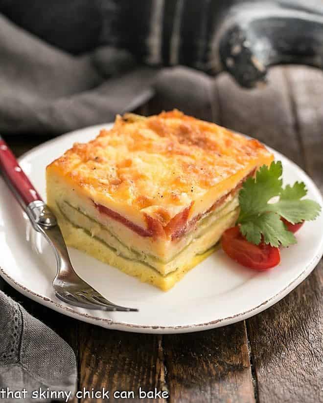 Chile Relleno Casserole slice on a white plate with cherry tomatoes and cilantro sprig.