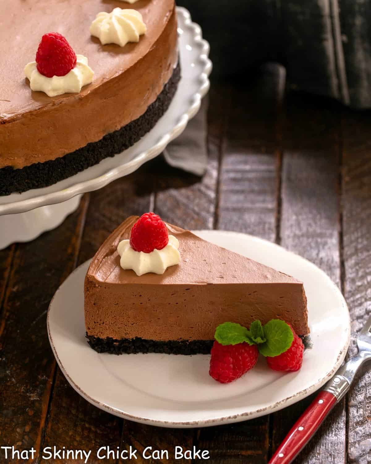 A slice of mousse cake on a white dessert plate in front of a cake stand.