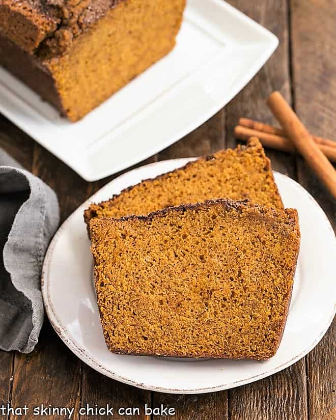 Slices of pumpkin bread on around white plate next to cinnamon sticks.