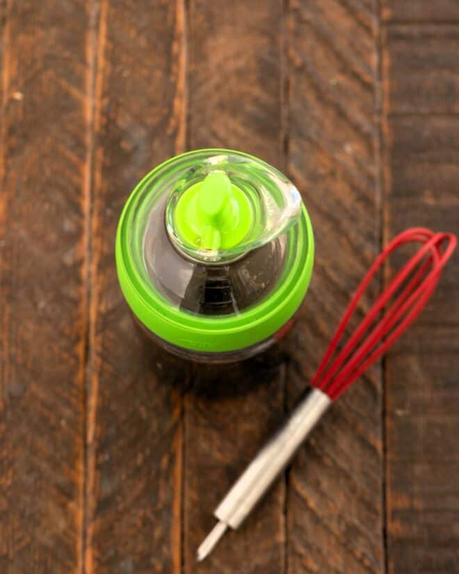 Spinach salad dressing in a carafe with a small whisk.