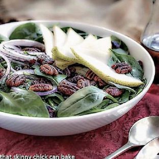Spinach Salad with Pears, Cranberries and Candied Pecans in a white ceramic serving bowl