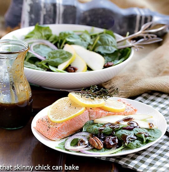Spinach Salad with Pears, Cranberries and Candied Pecans - Fabulous fall flavors in every bite of this tasty salad! Spinach Salad with Pears, Cranberries and Candied Pecans on a white plate with a salmon fillet