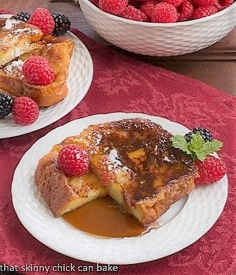 Sugar crusted slice of Frenc Toast cut in half on a plate with syrup and berries