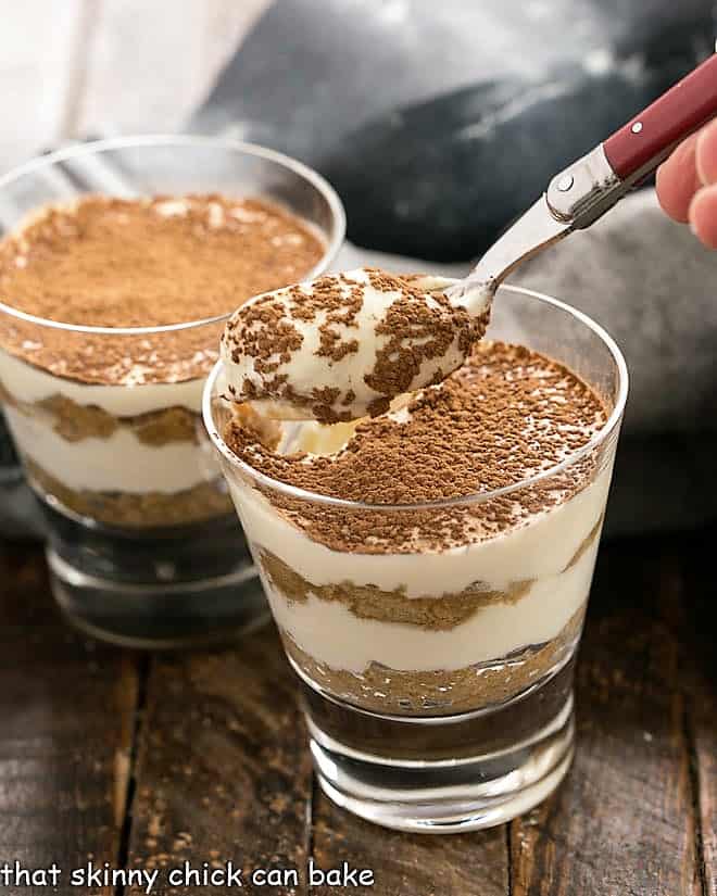 Two tiramisu parfaits and a red handled spoon with a spoonful of tiramisu.