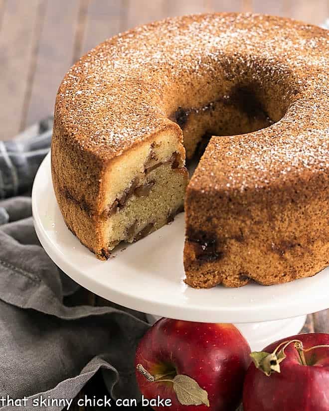Cinnamon apple bundt cake on a white cake stand with a slice removed.