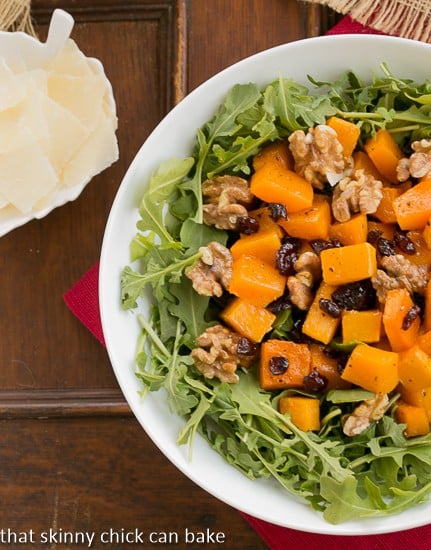 Arugula Salad with Roasted Butternut Squash from above in a white bowl with a side of Parmesan shavings.