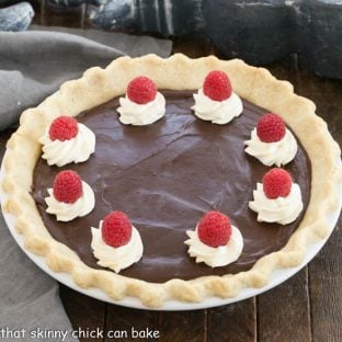 Overhead view of chocolate cream pie topped with whipped cream swirls, raspberries