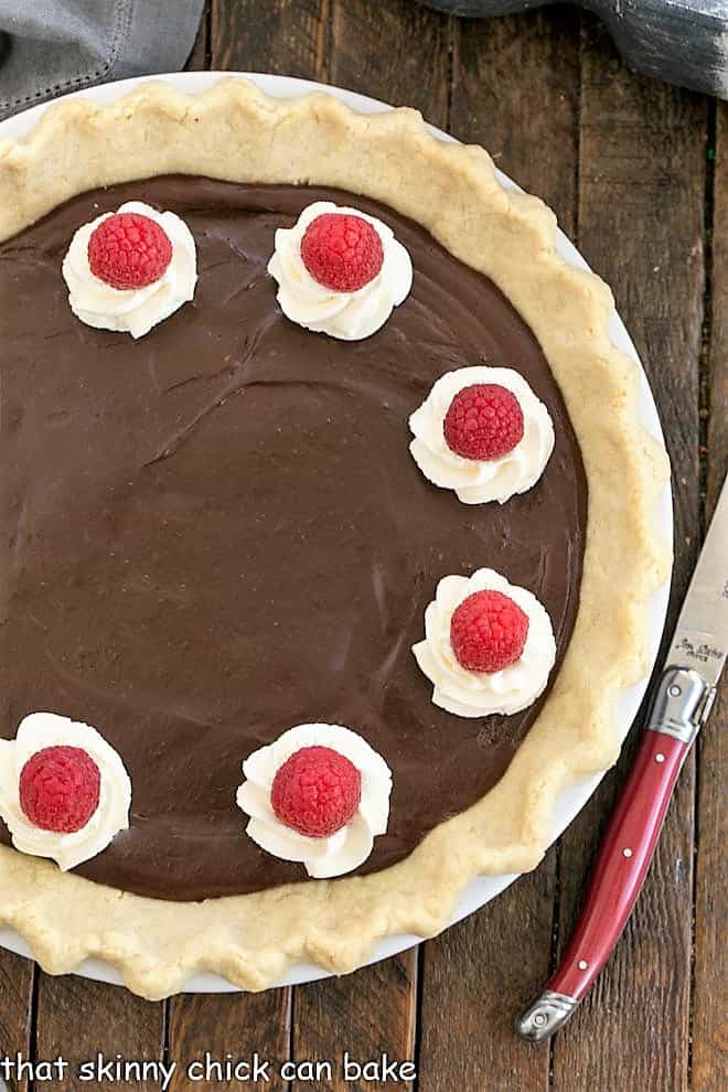 Overhead view of a chocolate cream pie with a red handled knife.