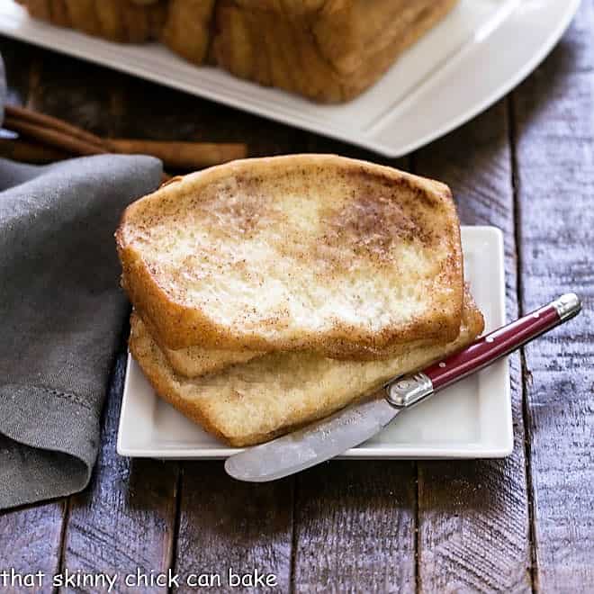 2 slices of cinnamon pull apart bread on a white plate with a red handle knife