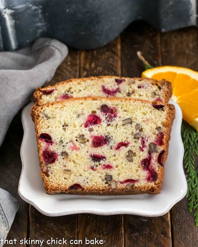 2 slices of cranberry bread on a white plate with an orange slice to garnish.