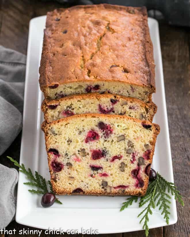Loaf of cranberry bread on a white tray with two slices in front of the loaf.