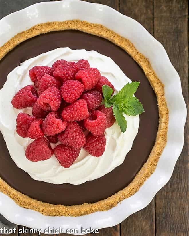 Overhead view of dark chocolate satin pie in a ceramic pie plate topped with raspberries and whipped cream.