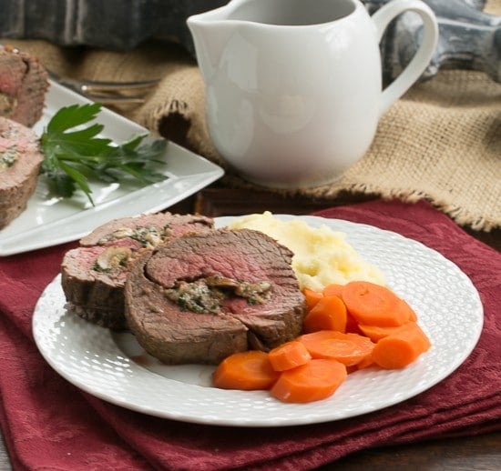 Gorgonzola and Mushroom Stuffed Beef Tenderloin on a dinner plate with carrots and mashed potatoes.