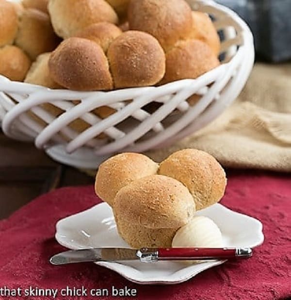 Honey Whole Wheat Cloverleaf Rolls in a basket behind one roll on a white plate.