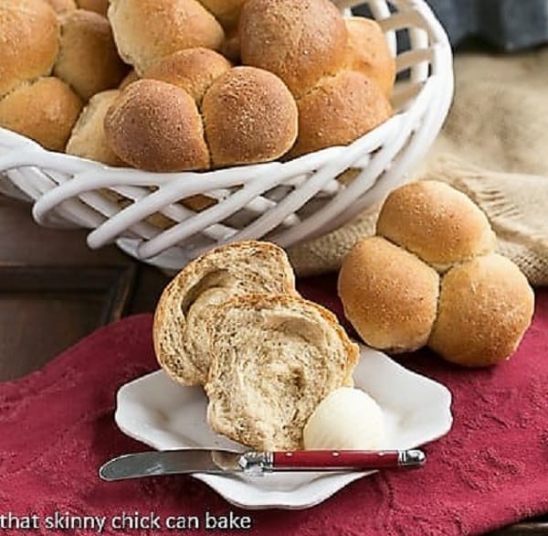 Honey Whole Wheat roll on a white plate, broken open with a pat of butter and a red handled knife